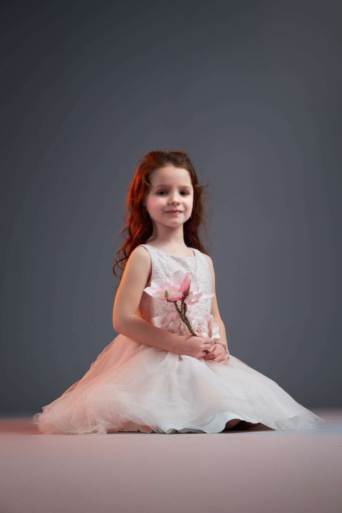 Studio protrait of a girl sitting on her knees posing with a flower.